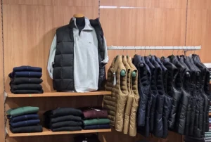 Felpa Lacoste grigia con mezza zip e gilet trapuntato nero su manichino, con gilet imbottiti e maglioni in esposizione